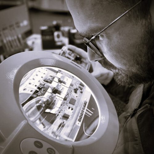 Ingenieur prüft elektronische Baugruppe unter einer Lupe im Elektroniklabor