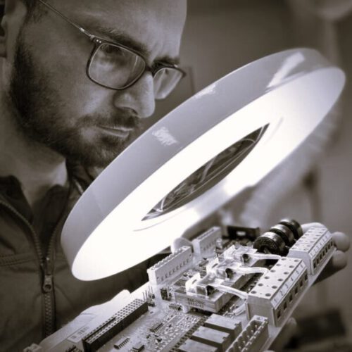 Ingenieur prüft elektronische Baugruppe unter einer Lupe im Elektroniklabor